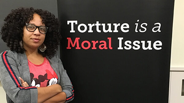 Solitary confinement survivor Nafeesah Goldsmith stands next to the words "torture is a moral issue."