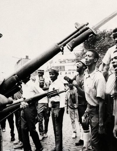 Photograph of Newarkers during the rebellion, who are facing national guard officers holding bayoneted guns.