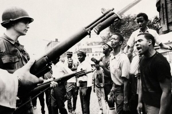 Photograph of Newarkers during the rebellion, who are facing national guard officers holding bayoneted guns.