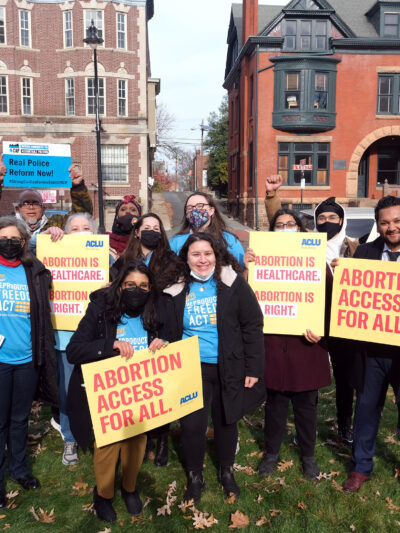 A group of people are standing with signs that read "abortion access for all" and "real police reform now"