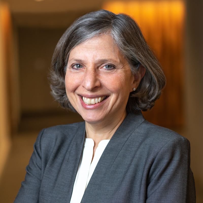 Catherine Weiss, a white woman with short grey hair wearing a grey suit jacket and a white shirt, smiles in a headshot portrait