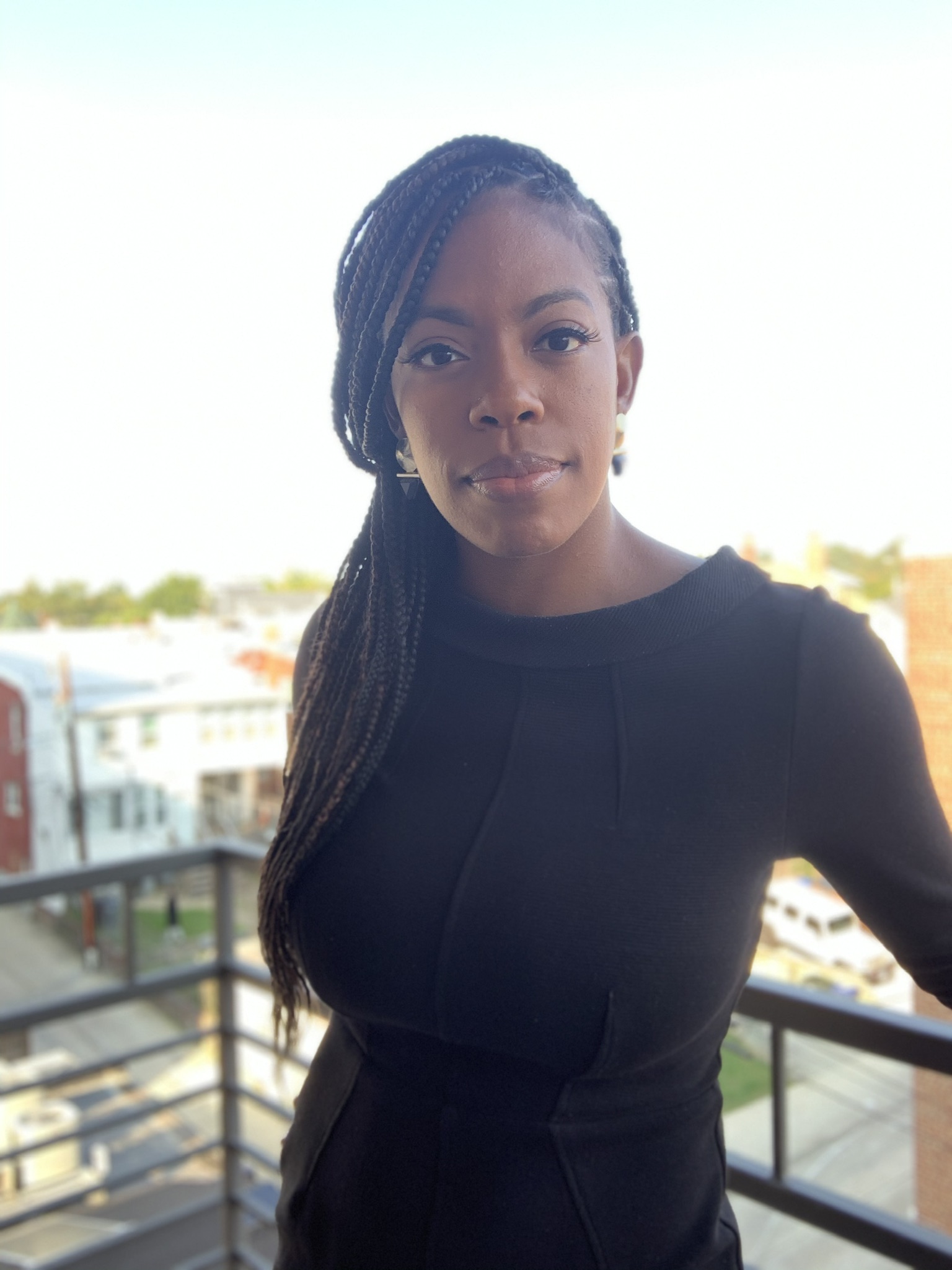 Lauren Johnson, a black woman with long braided hair that's gathered to one side, poses for a photo on a balcony.