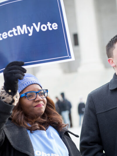 Black women wearing a light blue hat holding a sign saying "#ProtectMyVote