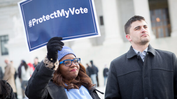 Black women wearing a light blue hat holding a sign saying "#ProtectMyVote