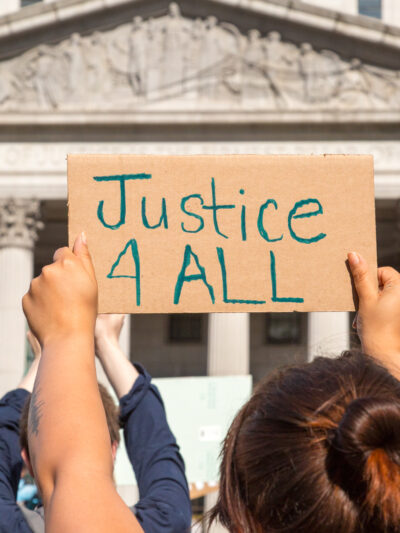 Protester holding sign reading "Justice 4 ALL" in front of state building