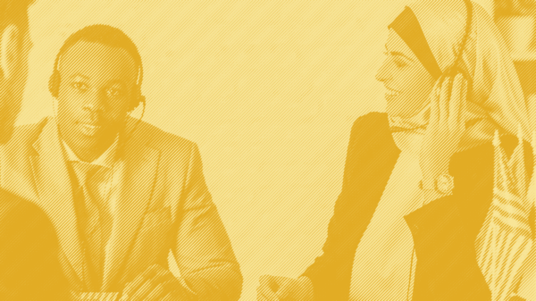 A man and a woman with headphones and mics sit at a table together with a yellow striped treatment applied
