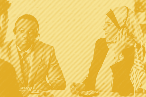 A man and a woman with headphones and mics sit at a table together with a yellow striped treatment applied