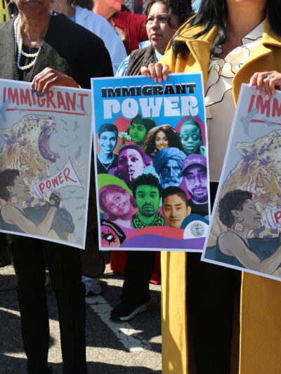 People hold signs that say "Immigrant Power" at a crowded rally.