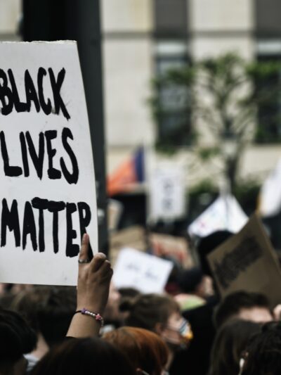 Black Lives Matter is handwritten in thick black on a white poster and held at a rally
