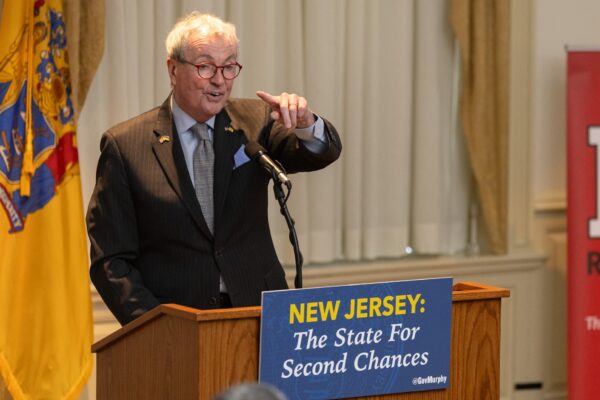 Governor Phil Murphy speaking at a podium with a sign that reads "New Jersey: The State for Second Chances"