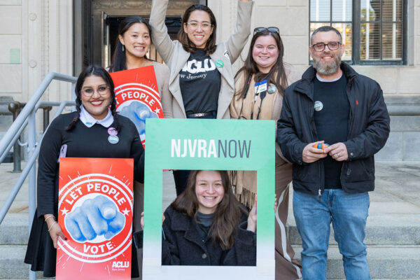 People stand on stairs holding signs that say "We the People" "NJVRA Now" and "Let People Vote"