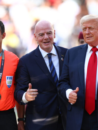 FIFA President Gianni Infantino and President Donald Trump pose with FIFA officials in bright orange referee jerseys and medals during the awards ceremony after Chelsea defeated Paris Saint-Germain 3–0 in the 2025 FIFA Club World Cup final at MetLife Stadium in East Rutherford, New Jersey.