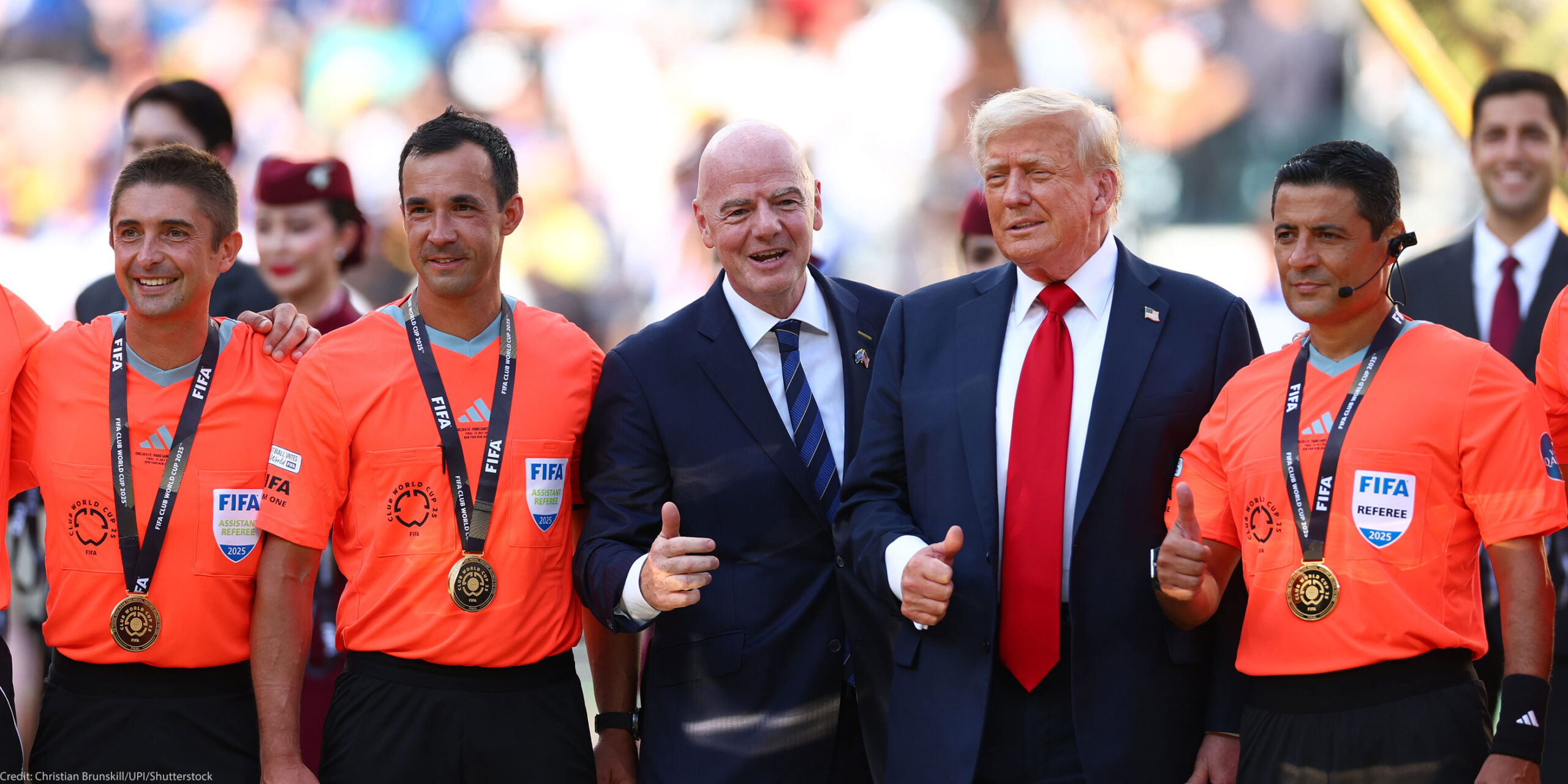 FIFA President Gianni Infantino and President Donald Trump pose with FIFA officials in bright orange referee jerseys and medals during the awards ceremony after Chelsea defeated Paris Saint-Germain 3–0 in the 2025 FIFA Club World Cup final at MetLife Stadium in East Rutherford, New Jersey.