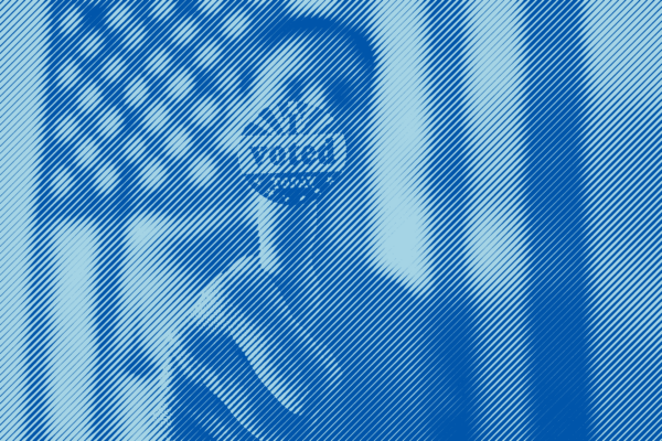 A man in front of an American flag holding an "I voted" sticker