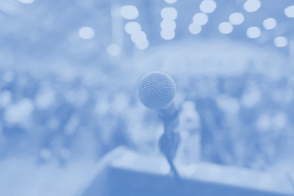 A mircophone on a podium with a crowd of people in the background with a blue strip treatment