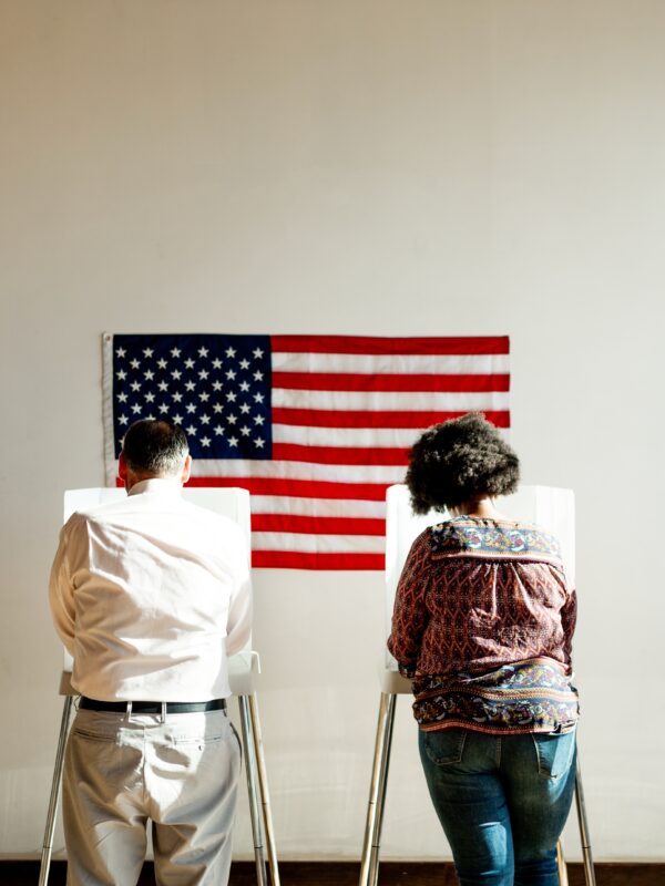 A group of people voting in polling booths with an American Flag behind them