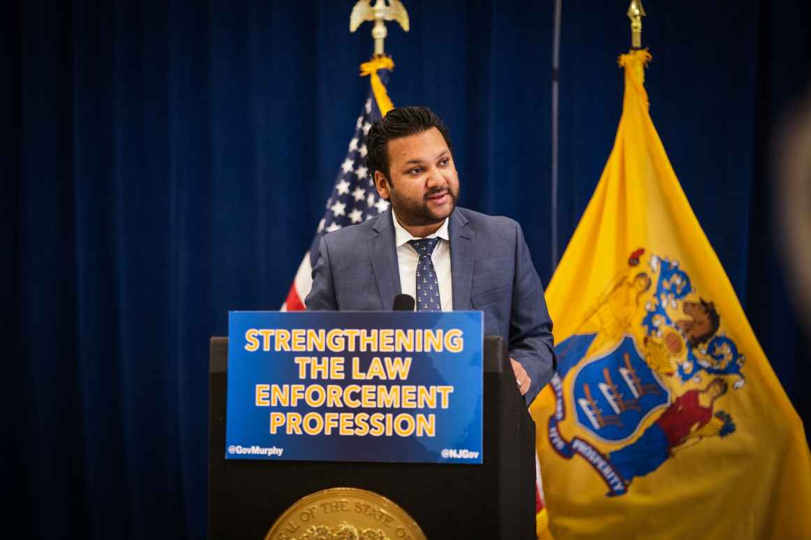 A man in a suit is standing and speaking behind a podium with a sign that reads "Strengthening the law enforcement profession"