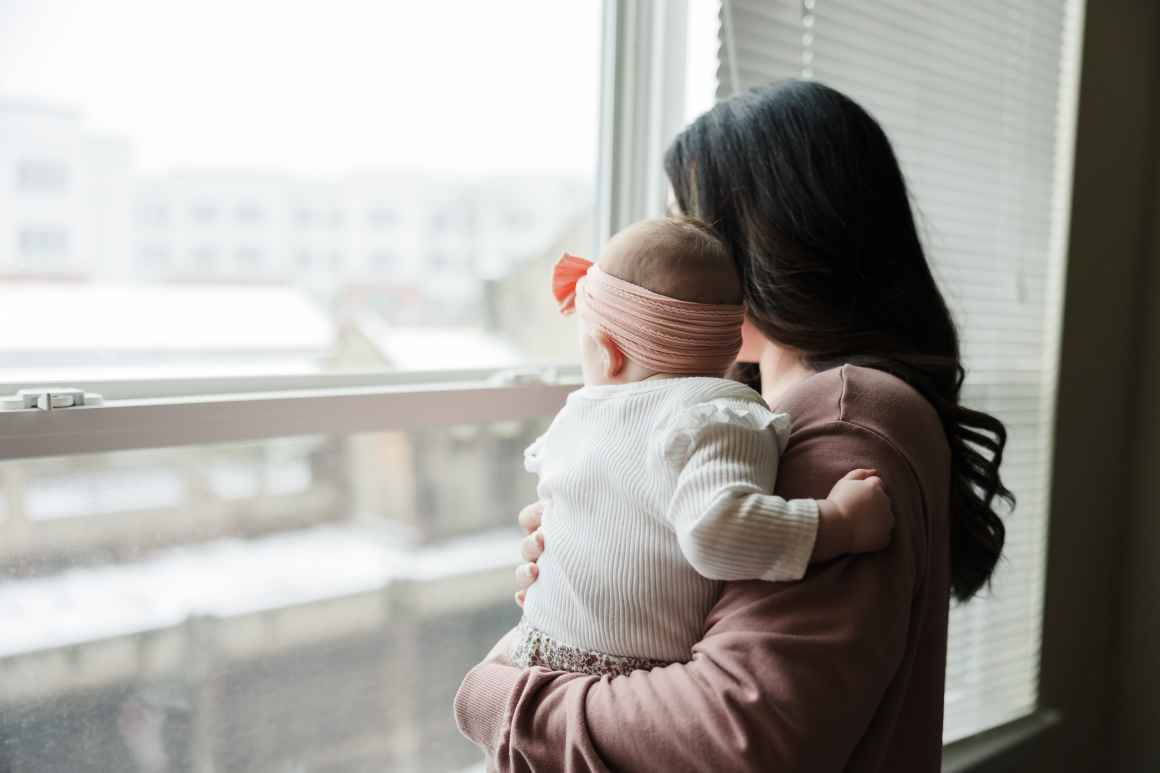 A woman holds a baby while looking out a large window