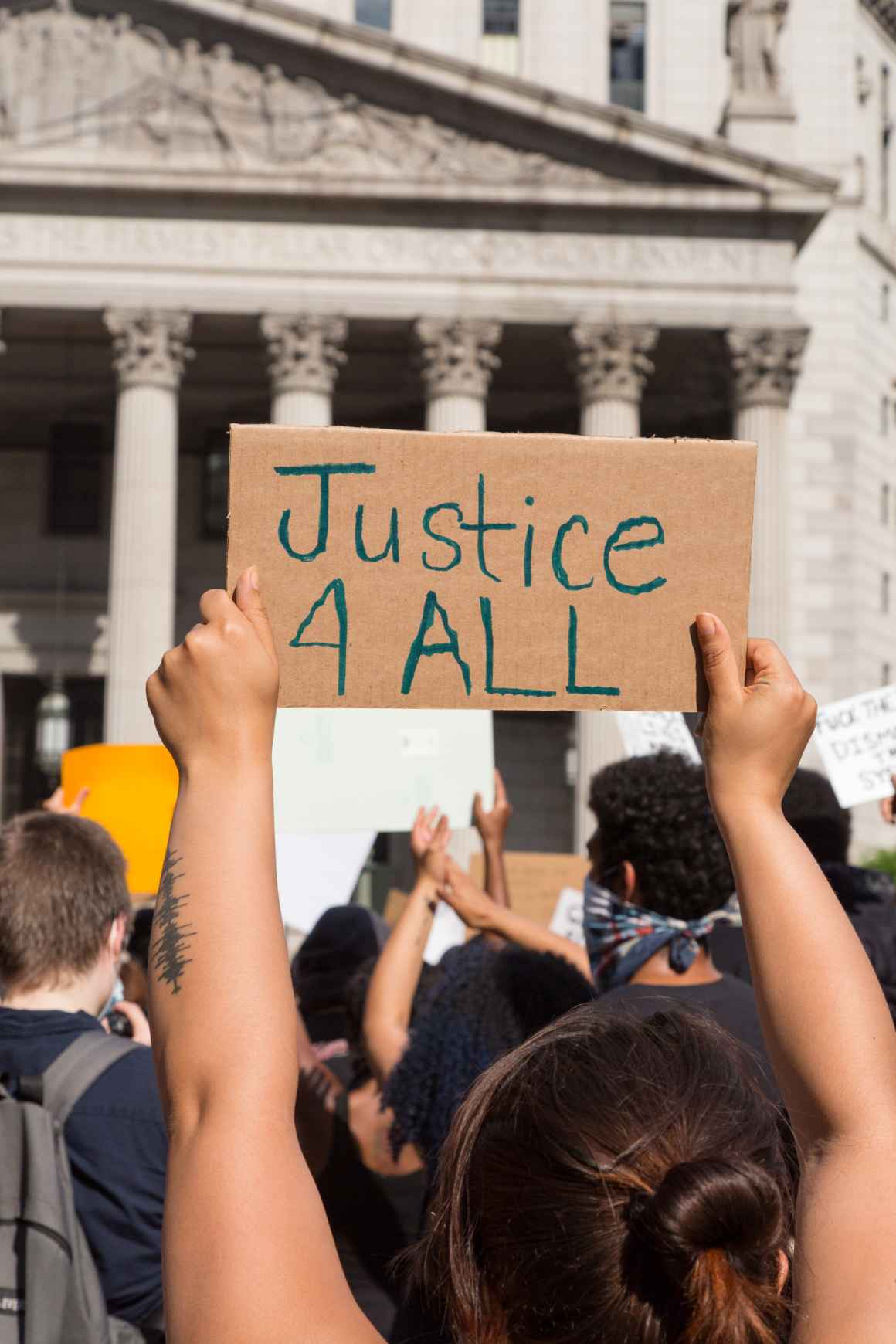 Hands holding up a sign with word "Justice 4 ALL" in front of a court house
