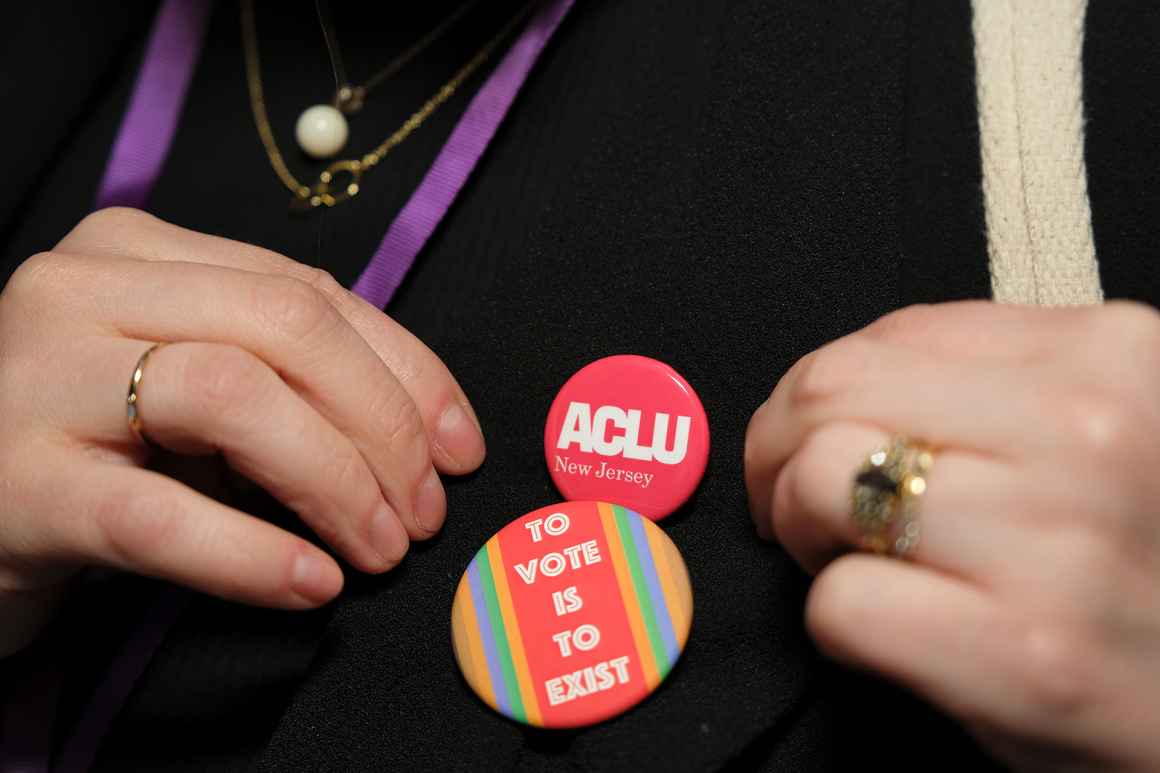 Hands holding a shirt that has a pin reading "To Vote is To Exist"