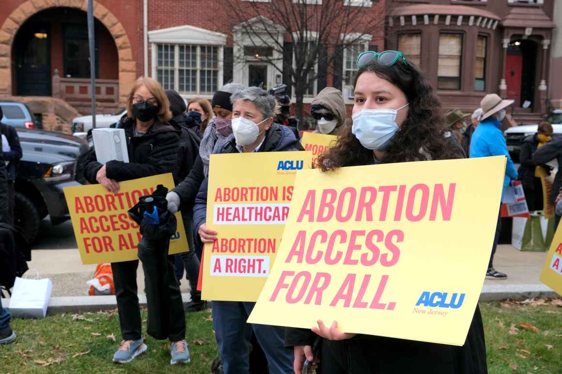 A group of masked protesters are holding signs that read: "Abortion access for all" and "abortion is healthcare, abortion is a right."