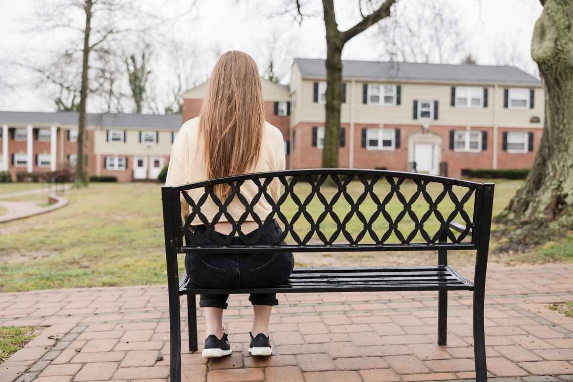 a woman with long hair is sitting on a bench overlooking a row of houses