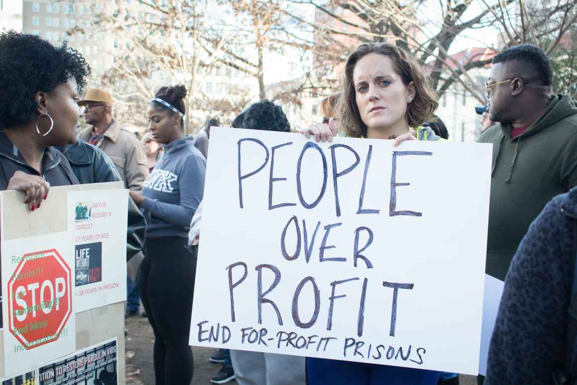 white woman holding a protest sign reading "people over Profit" 