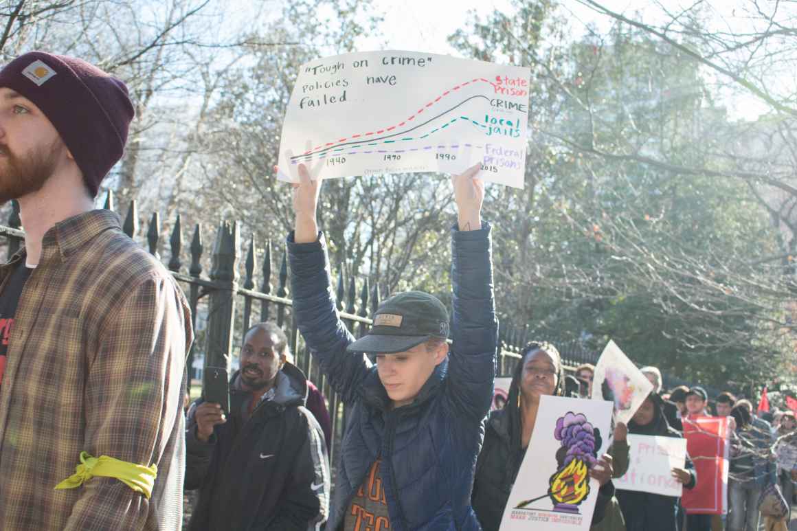 Woman in hat with blue jacket holding up a protest sign in a crowd