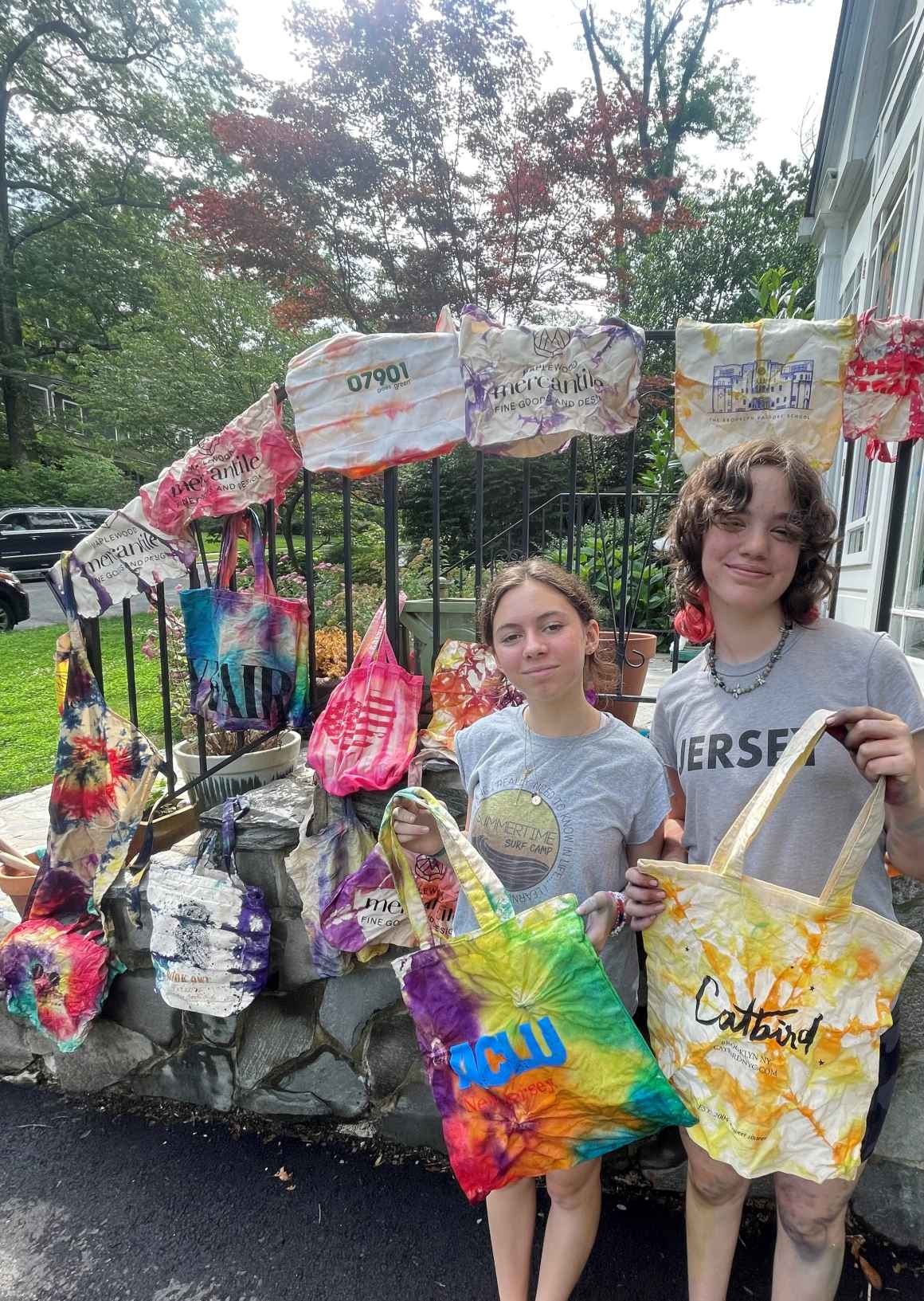 Two young white girls with brown hair pose with tie dyed bags they created