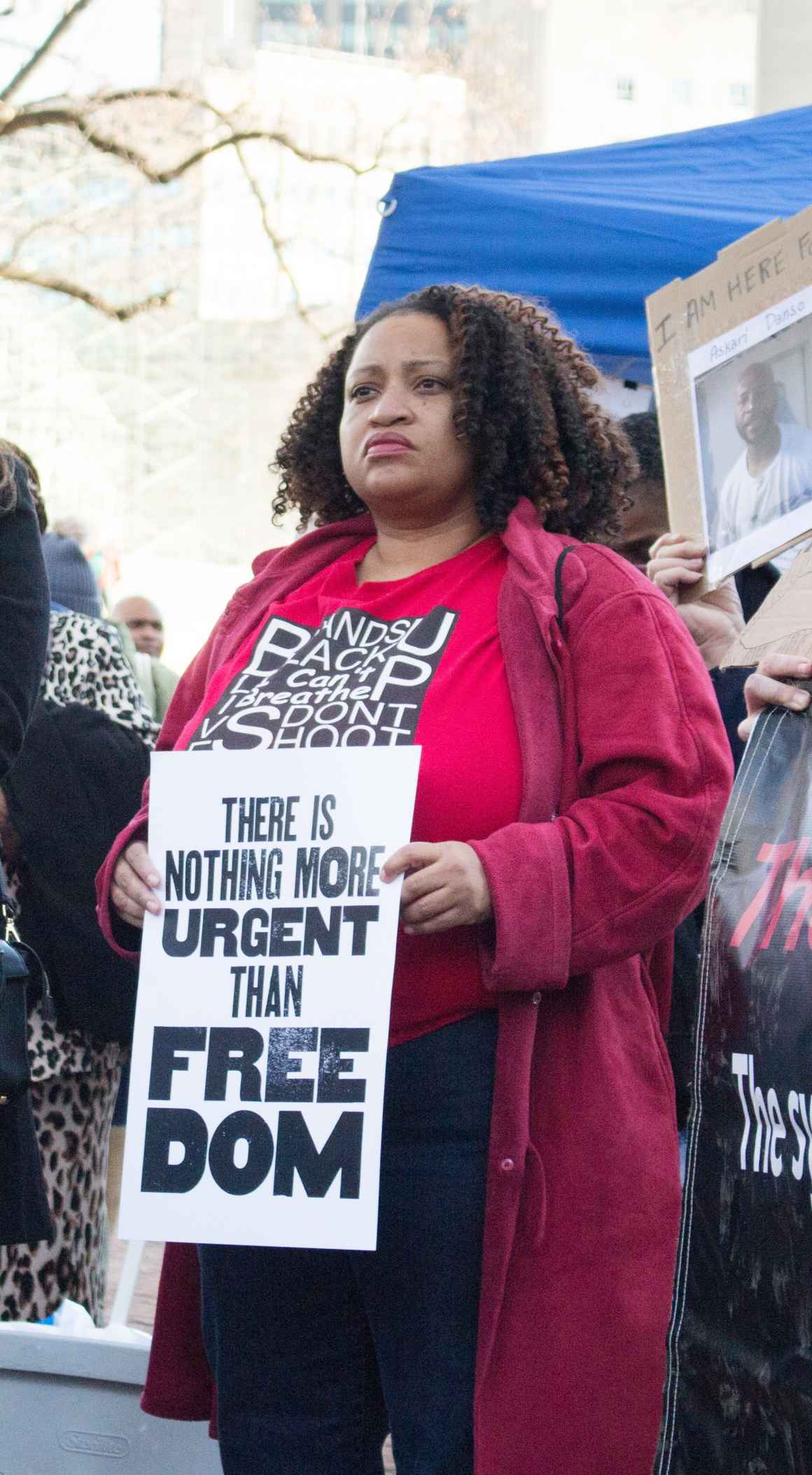 Black woman holding sign amidst protest reading "there is nothing more urgent than freedom"