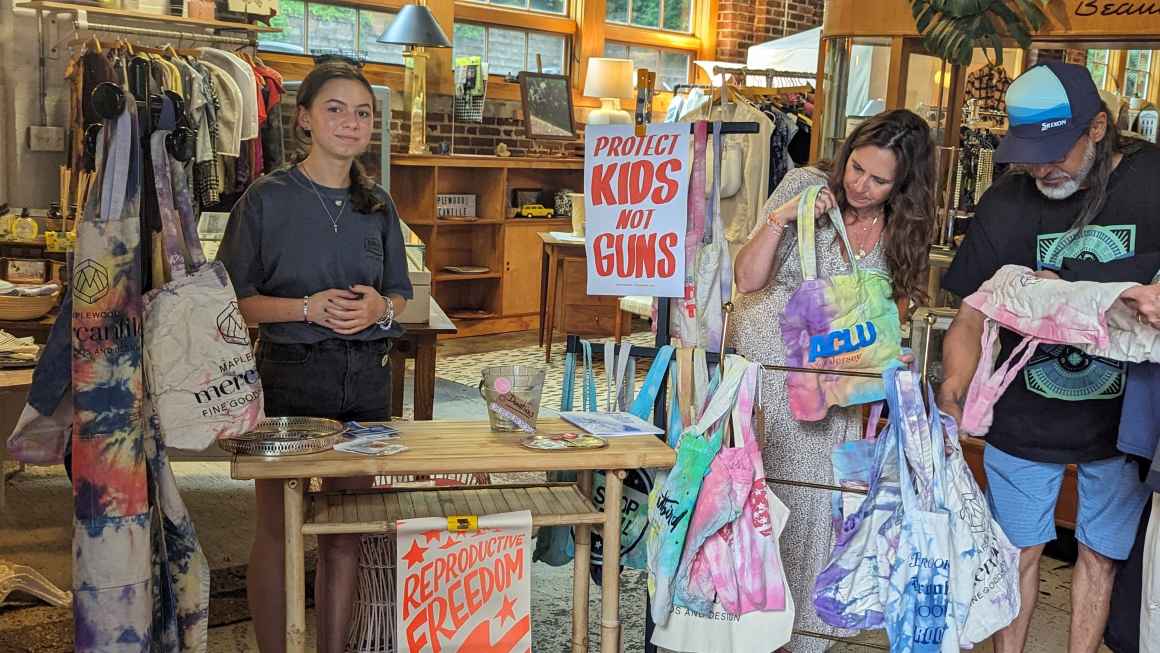 Young white girl with grey tshirt posing with handmade dyed bags in a store