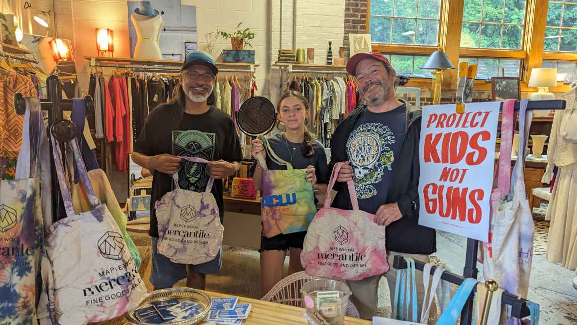 Young woman stands with two middle age men holding hand dyed tote bags in a store