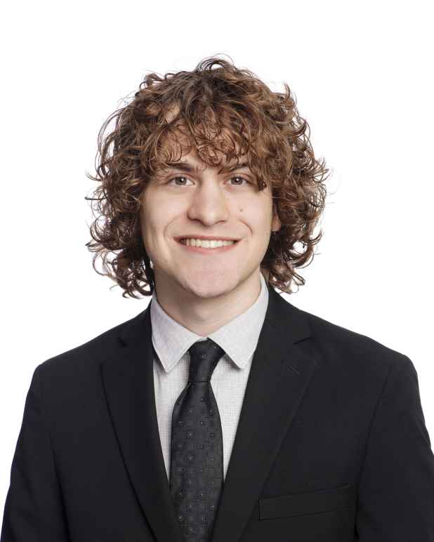 White man with brown curly hair wearing a black suit against a white background