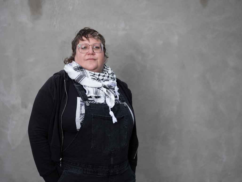 White woman wearing a black shirt and a scarf standing in front of a grey background