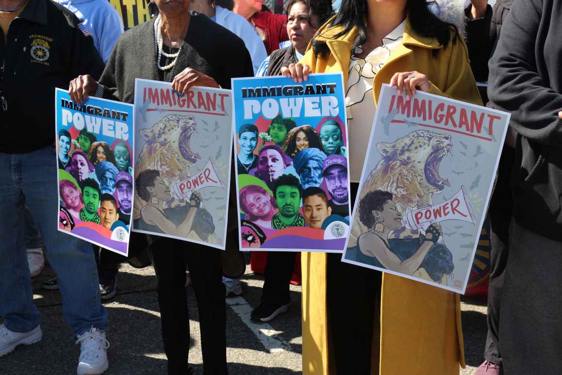 People hold signs that say "Immigrant Power" at a crowded rally.