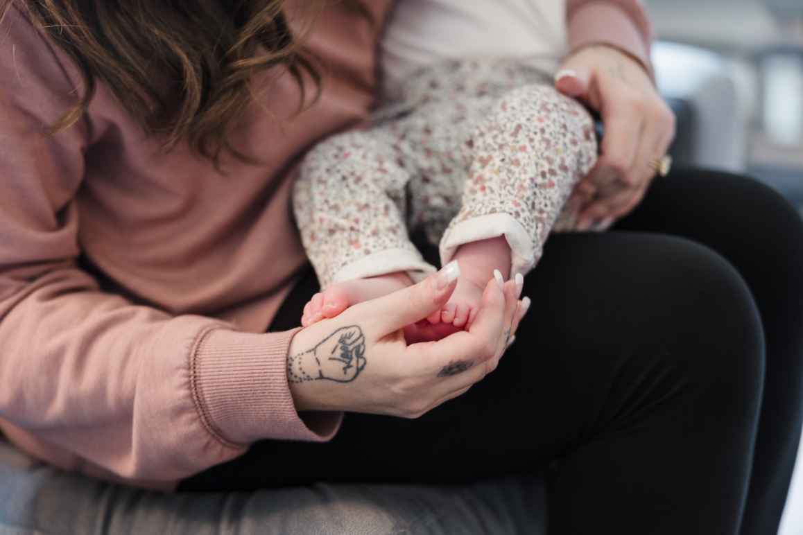 a woman cradles a baby in her arms, touching the baby's feet