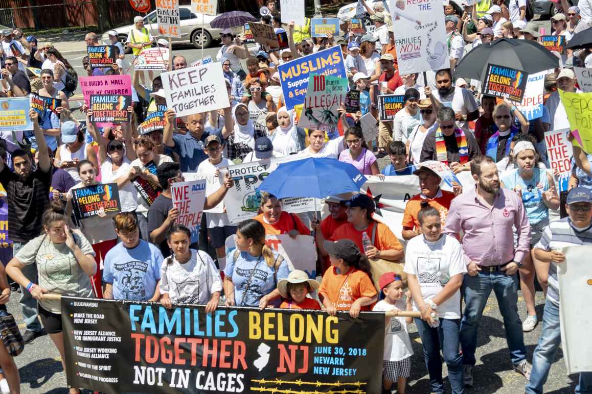 Group of protesters marching with banner reading "Families Belong Together. Not in Cages." 