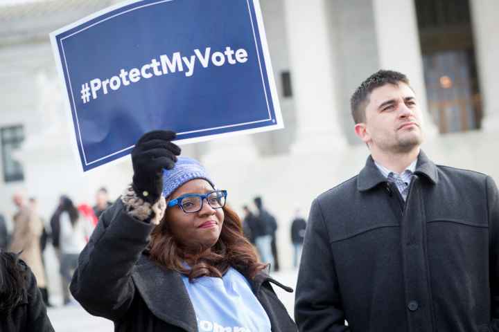 Black women wearing a light blue hat holding a sign saying "#ProtectMyVote