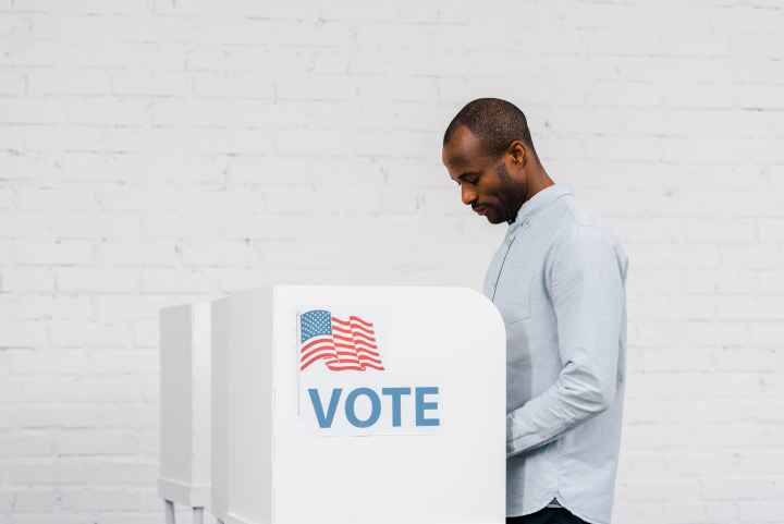Black Man voting against a white brick background