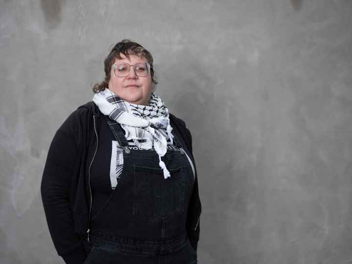 White woman wearing a black shirt and a scarf standing in front of a grey background