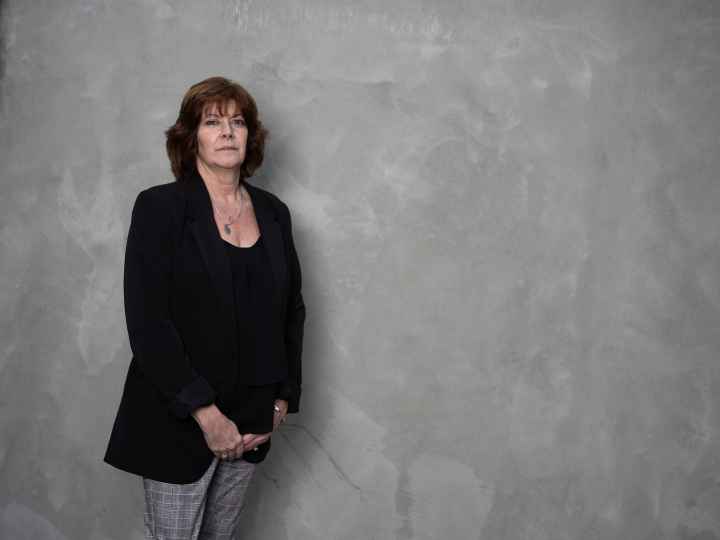 White women wearing a black blazer and grey pants in front of a grey background