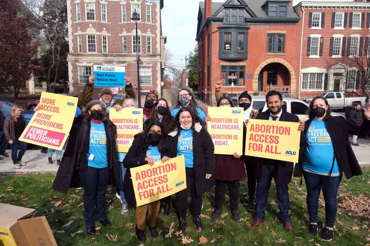 A group of people are standing with signs that read "abortion access for all" and "real police reform now"