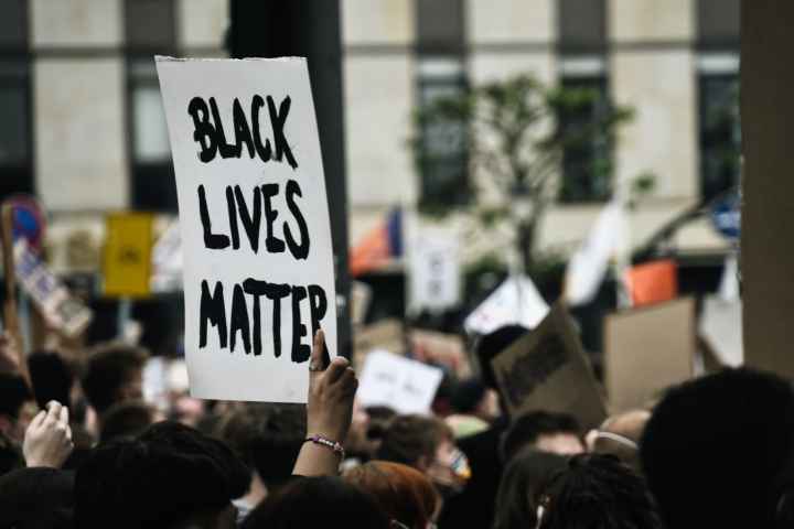 Black Lives Matter is handwritten in thick black on a white poster and held at a rally