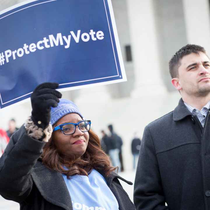 Black women wearing a light blue hat holding a sign saying "#ProtectMyVote