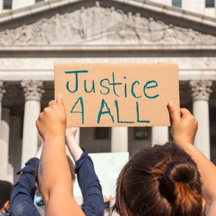 Protester holding sign reading "Justice 4 ALL" in front of state building