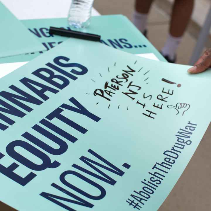 A mint green sign reads: Cannabis equity now. Hashtag Abolish the Drug War. A handwritten note is written off the side that reads: Paterson NJ is here!