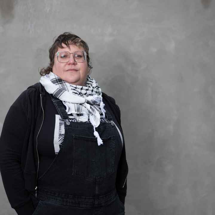 White woman wearing a black shirt and a scarf standing in front of a grey background