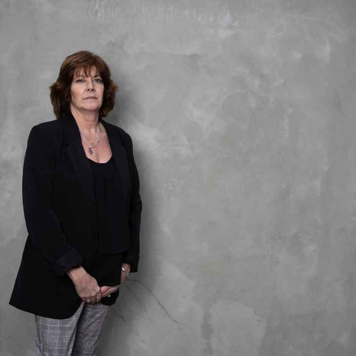 White women wearing a black blazer and grey pants in front of a grey background