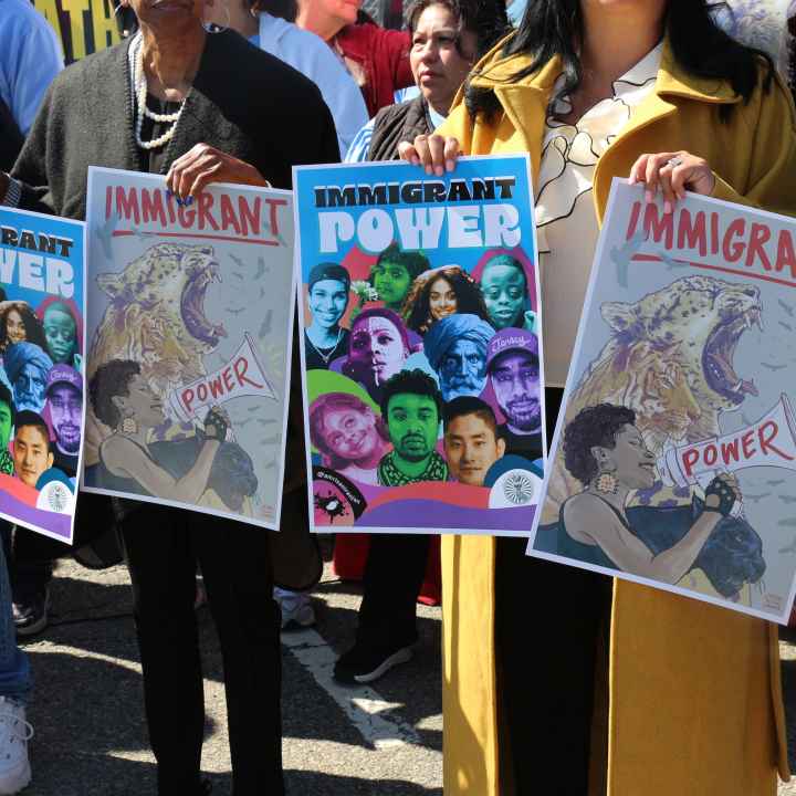 People hold signs that say "Immigrant Power" at a crowded rally.