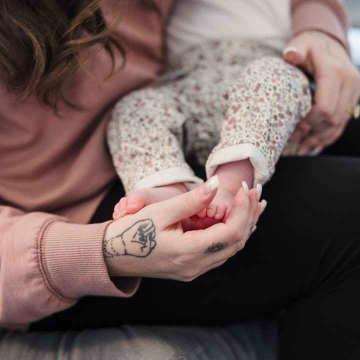 a woman cradles a baby in her arms, touching the baby's feet